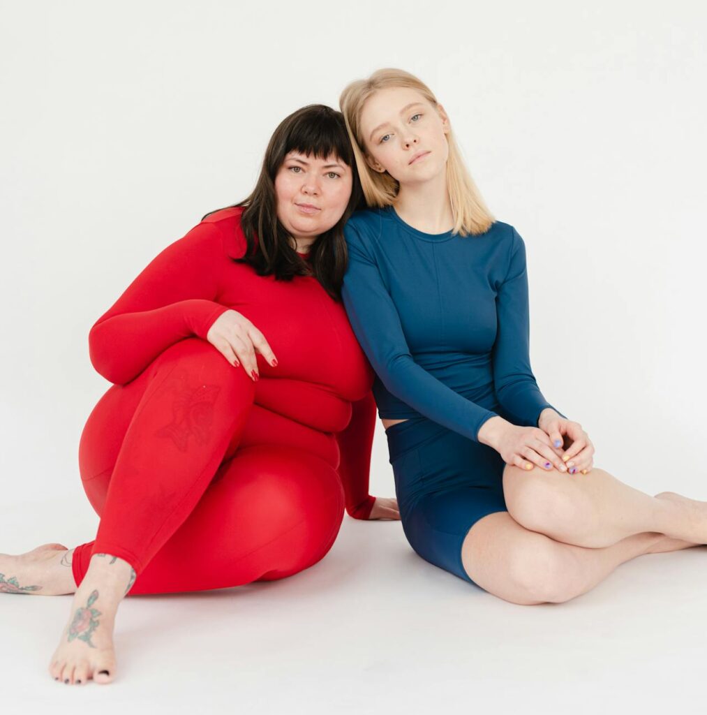 zwei Frauen mit unterschiedlichem Gewicht sitzen Kopf an Kopf nebeneinander.