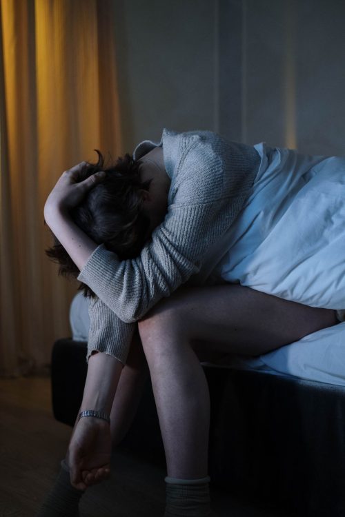 Schlaflos - eine Frau sitzt am Bettrand und ist verzweifelt weil sie nicht schlafen kann.