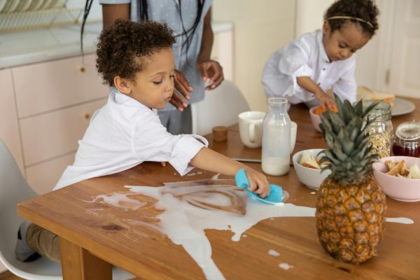 Kind wischt verschüttete Milch auf Tisch auf